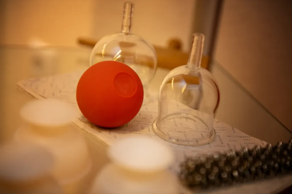 Glasglocken für eine Schröpfmassage liegen auf einem Papier, die Lichtstimmung ist warm und orange.