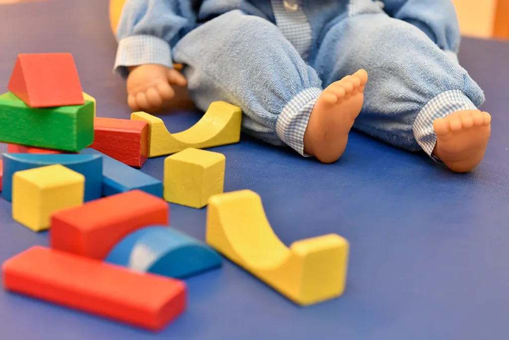 Fußbereich einer sitzenden Puppe und bunte Bausteine auf einem blauen Boden.