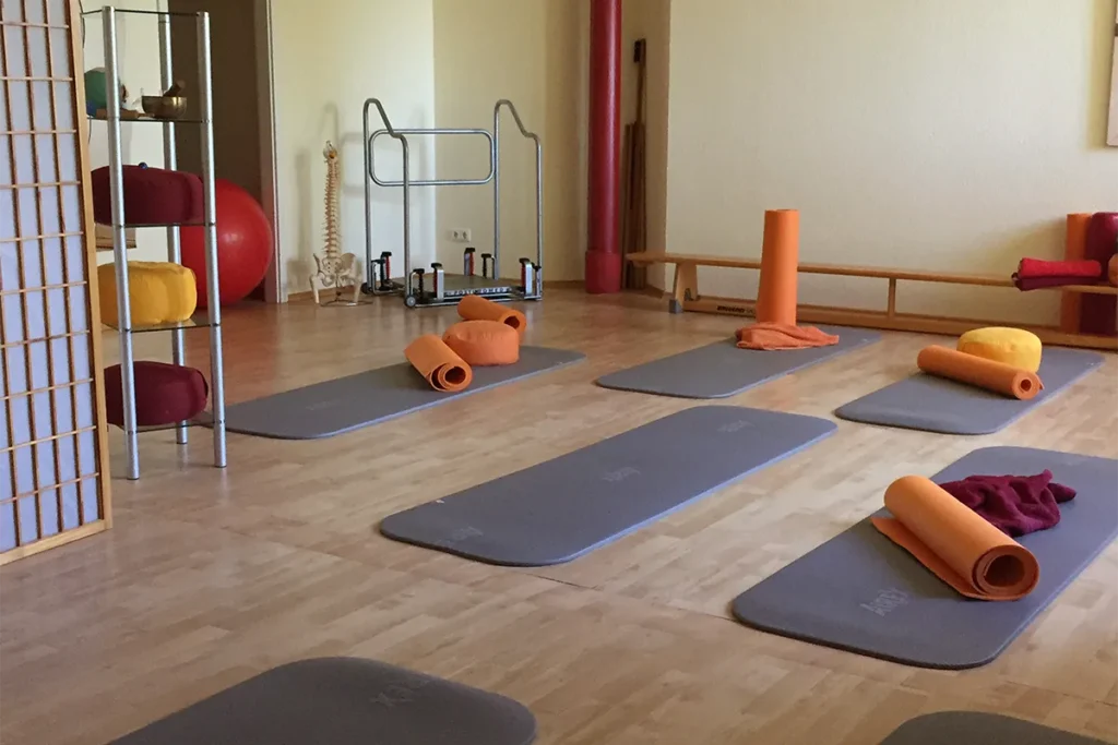 Kursraum für Pilates mit Boden in Parkett-Optik auf dem dunkelgraue Matten liegen.